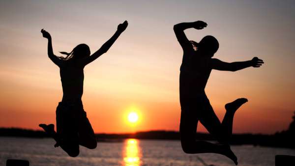 Siluetter av två personer som hoppar ned i vatten i solnedgång