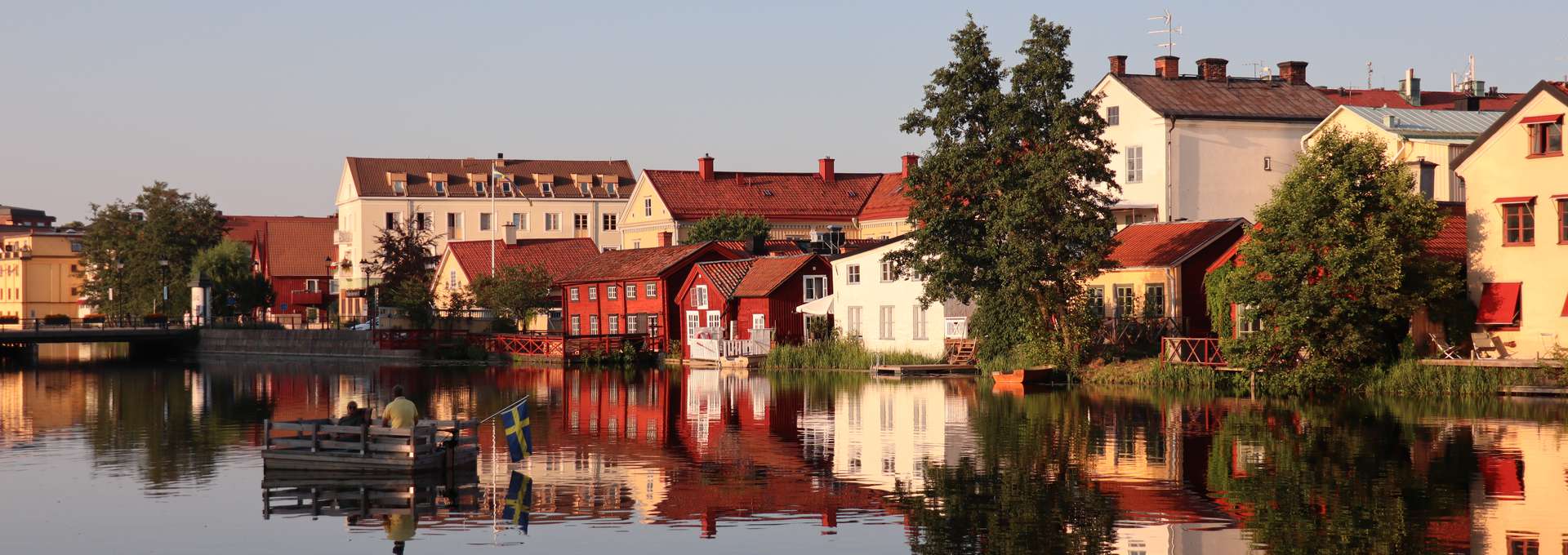 I Eskilstunaån åker en bryggflotte och i bakgrunden ser man Gamla staden med sina gamla hus